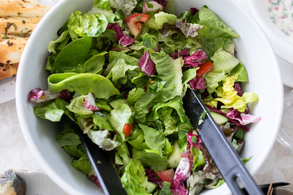 A bowl of salad leaves with a pair of tongs