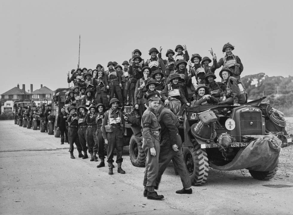 A British Military Policeman stands by as a motorised column of British 2nd Army soldiers giving the V for Victory sign
