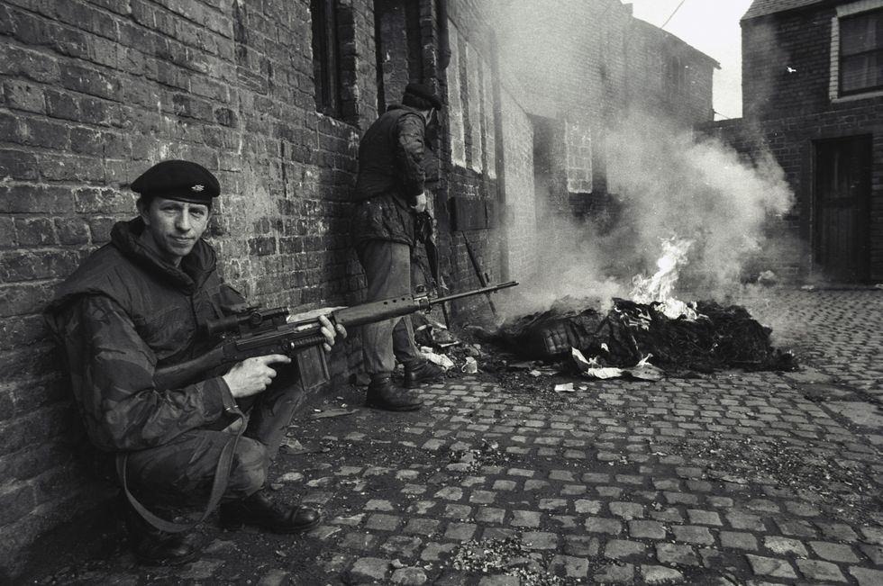 A British soldier provides cover for his fellow soldiers while they check out a burning building
