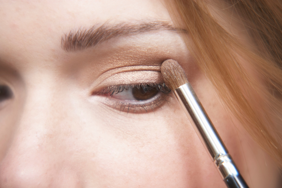 A brown-eyed woman applies a neutral-toned eyeshadow