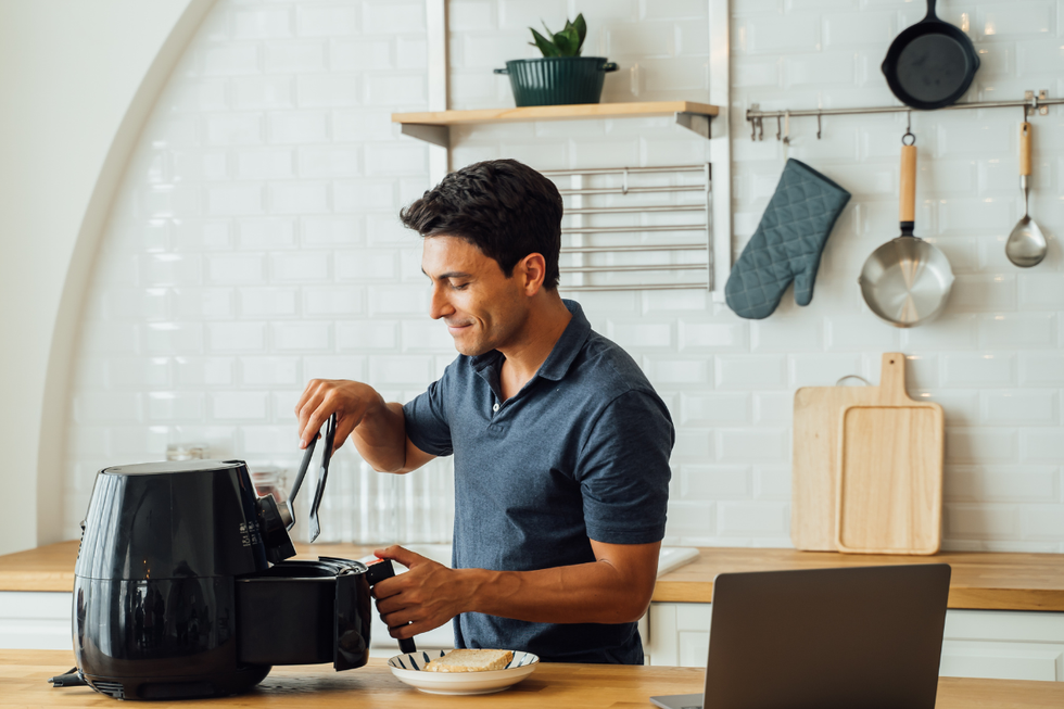 A brunette man using a black airfryer, wearing a blue short-sleeved shirt in a kitchen