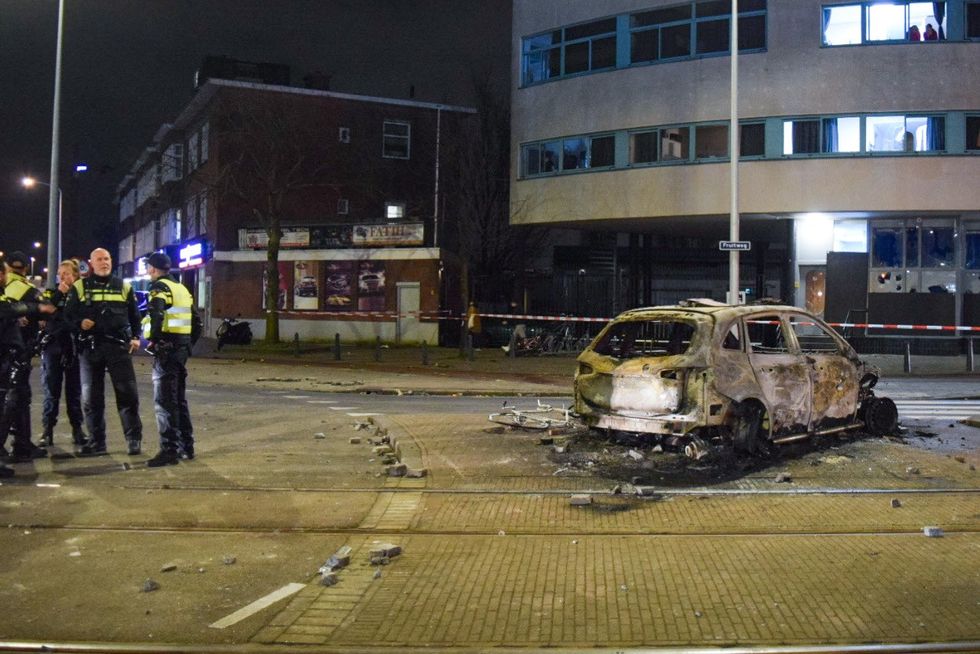 A burned vehicle is seen near police officers at the Opera hall center on the Fruitweg following clashes between two groups of Eritreans during riots