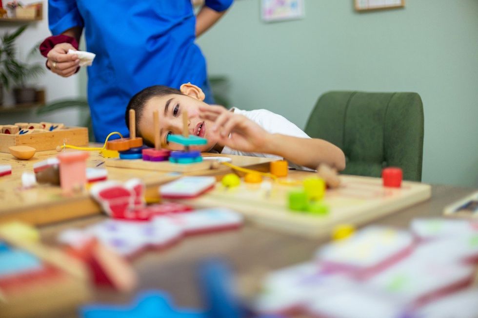 A caring nurse guides a little boy with autism through a series of sensory exercises, fostering his motor coordination using a variety of vibrant toys