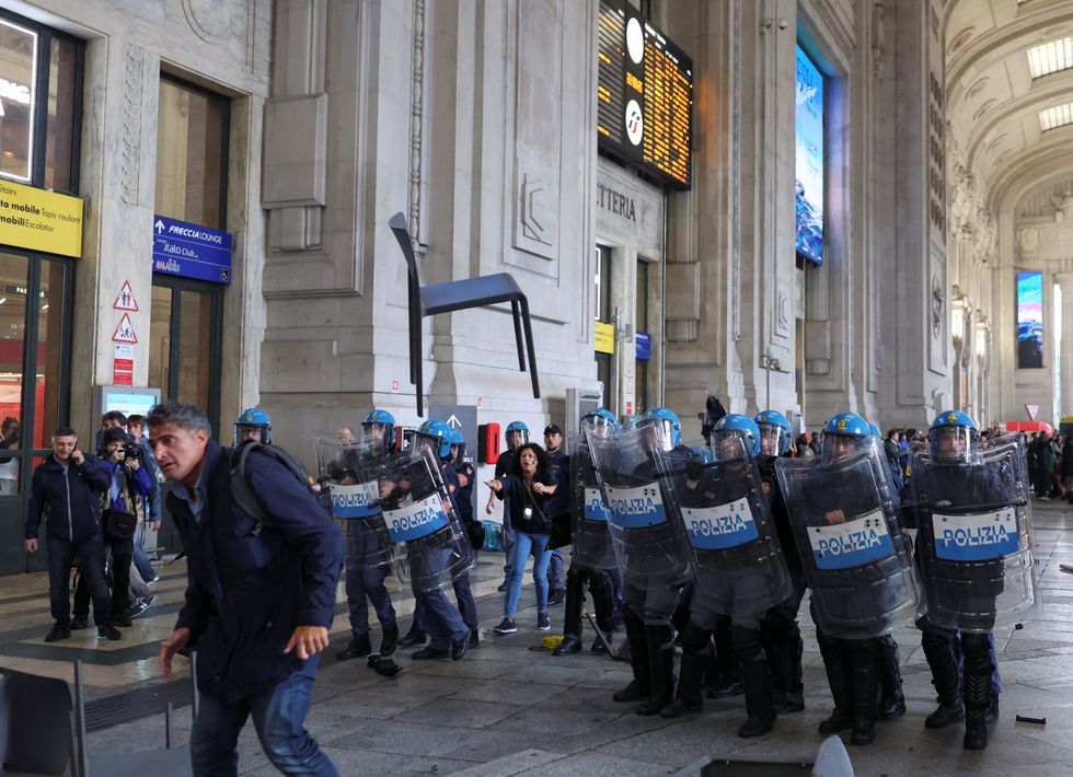 A chair flies through the air as riot police watch on inside Milano Centrale station