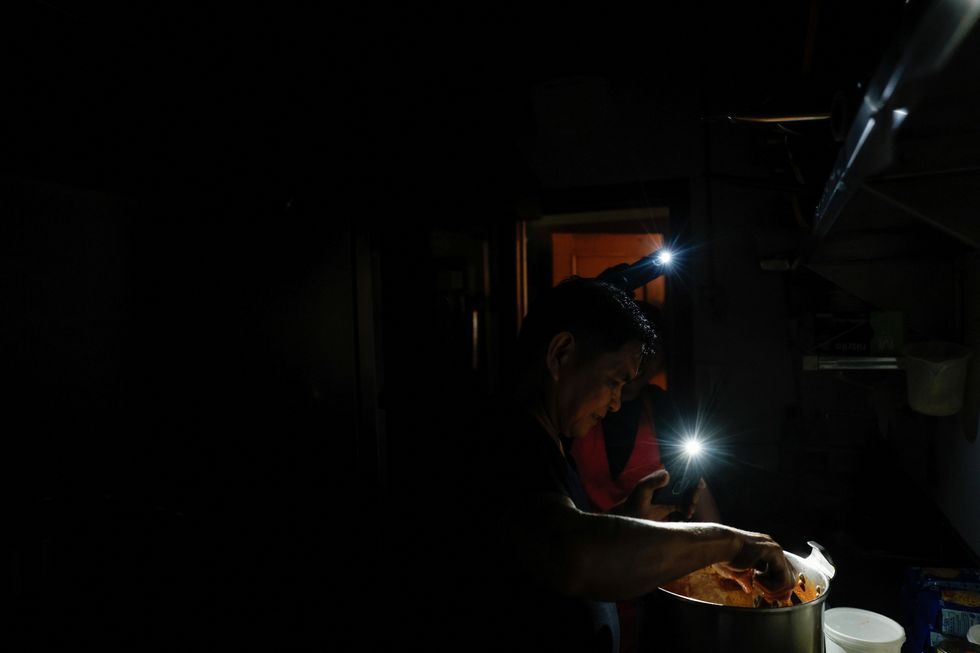 A chef at La Cocinona restaurant works in a dark kitchen with the aid of phone flashlights during a power outage in Madrid