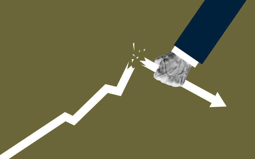 A conceptual image depicting a human hand breaking an upward-pointing graph line.
