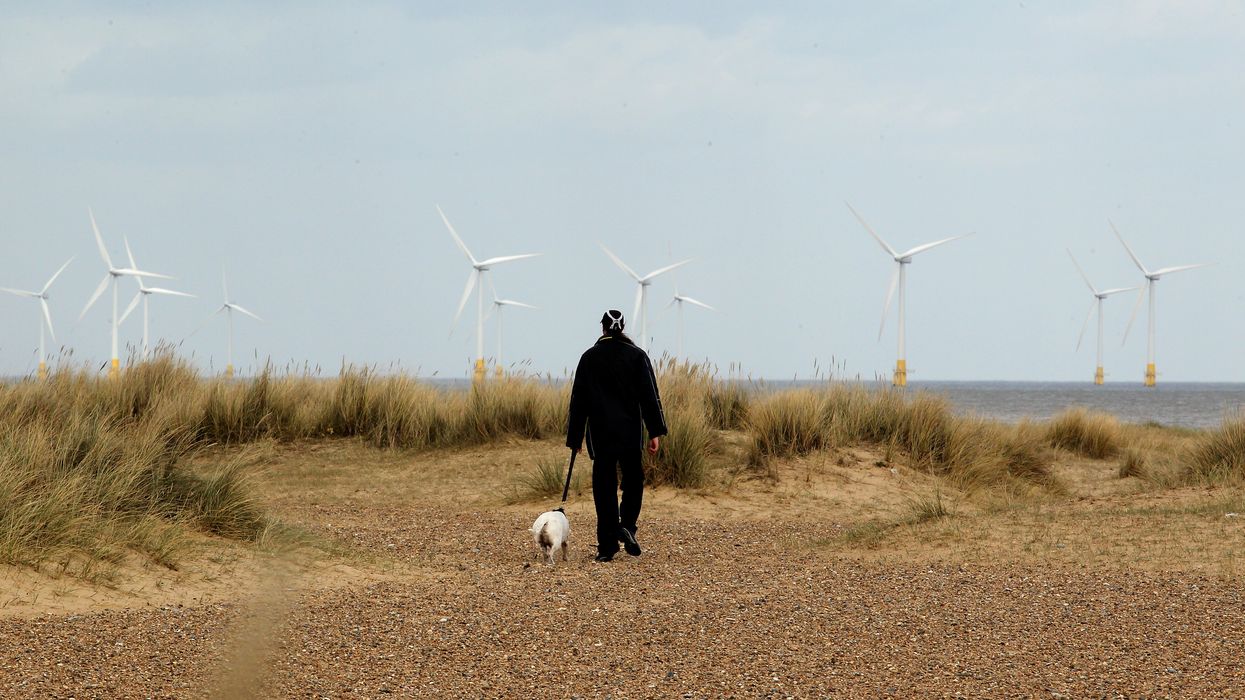 A dog walker on the sand dunes passes offshore wind turbines in the Norfolk seaside town of Great Yarmouth