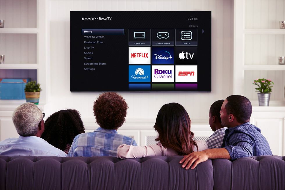 a family sit around on a sofa and watch a wall-mounted flatscreen tv running roku software