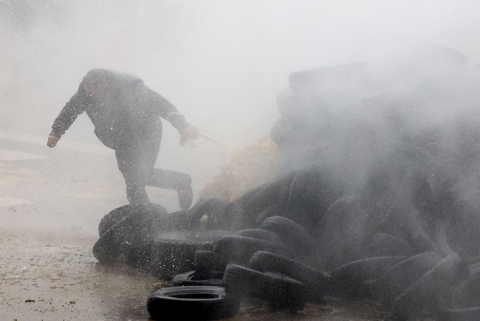 A farmer runs behind tires as he is sprayed by a water cannon during a protest of European farmers