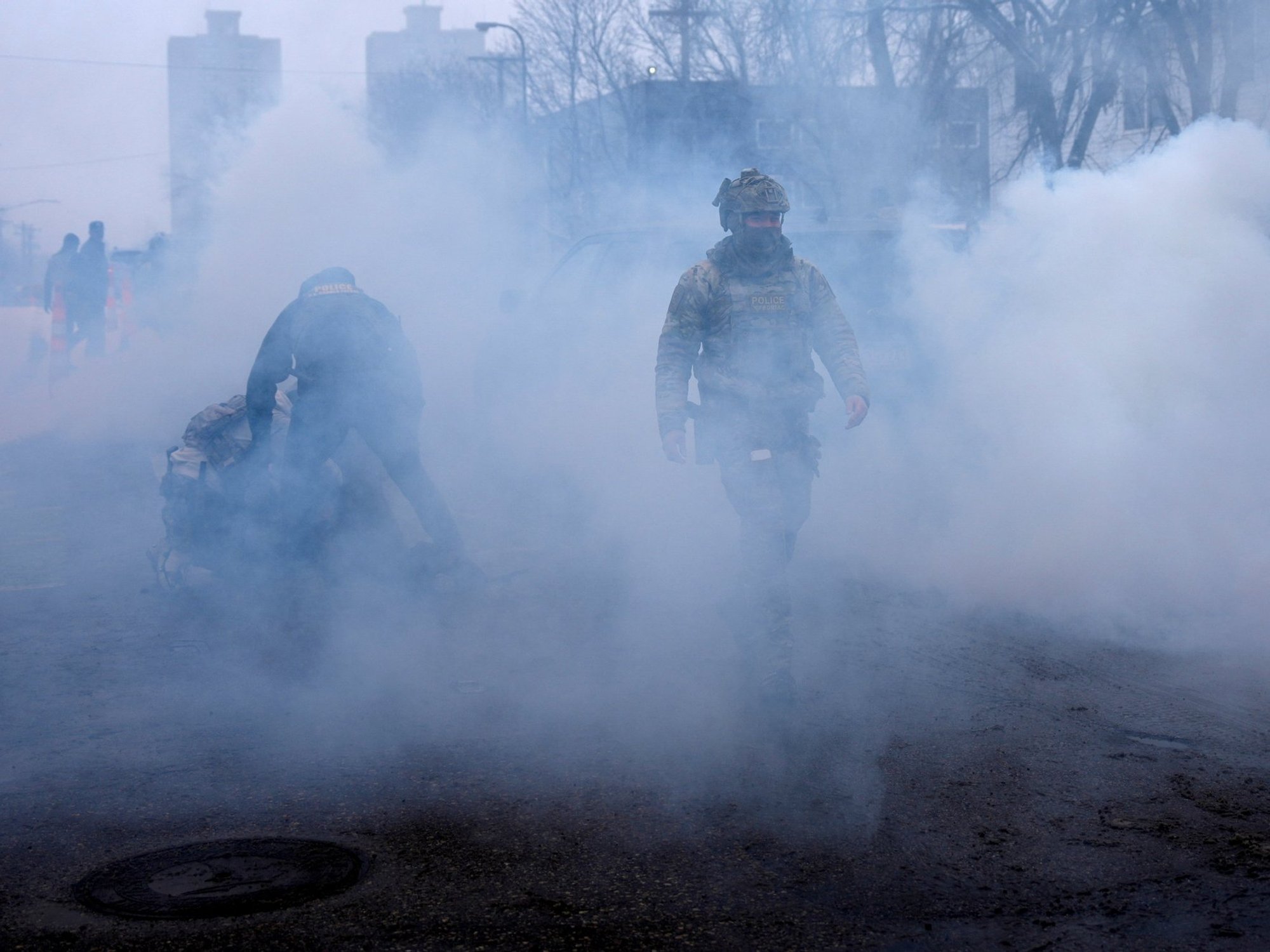 A federal agent walks as others hold a person down while being surrounded by tear gas used to deter protesters,