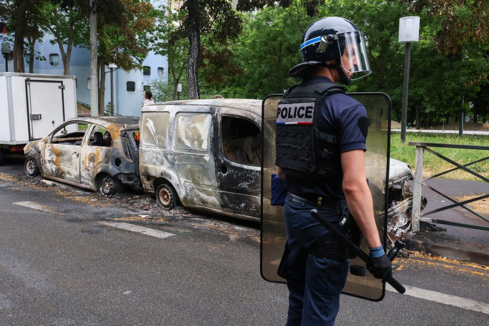 A French police officer stands guard next to vehicles burnt during a night of clashes between protesters and police