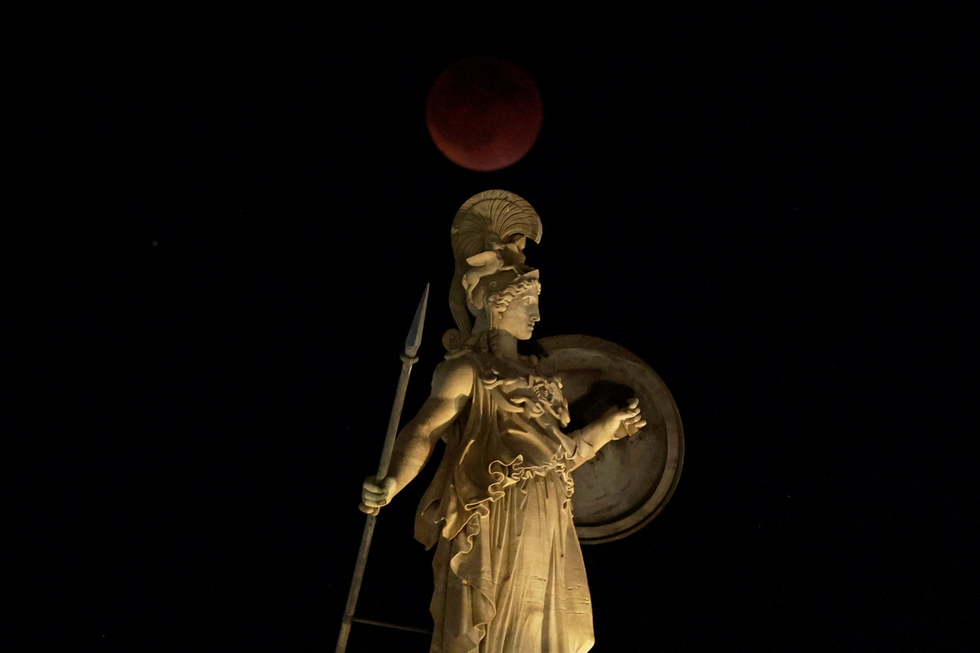 A full moon rises during an eclipse behind the statue of ancient Athena goddess in Athens, Greece