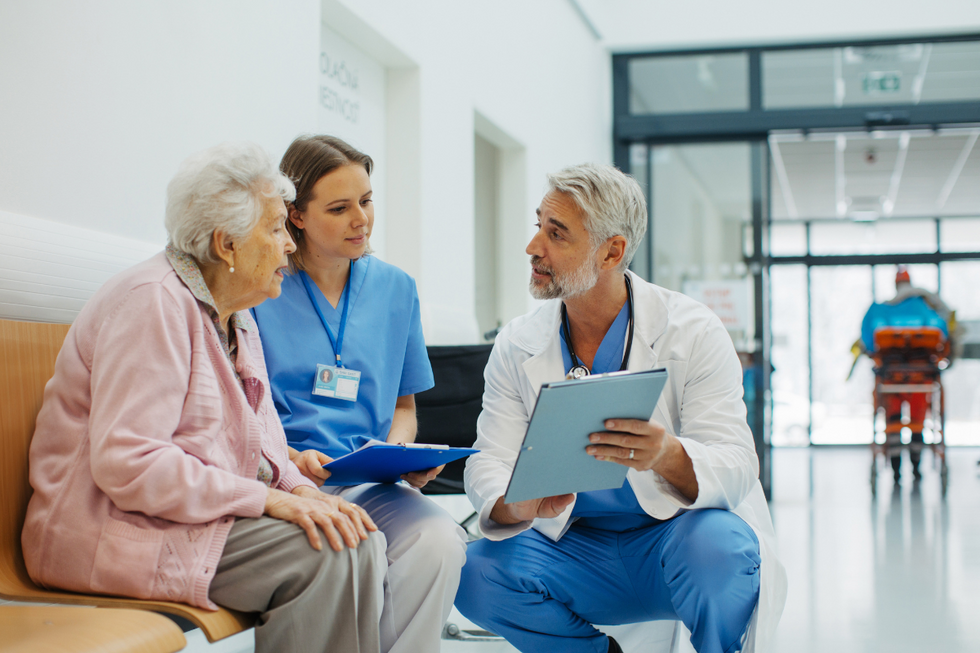 A grey-haired doctor showing an elderly woman her chart, next to a younger brunette doctor