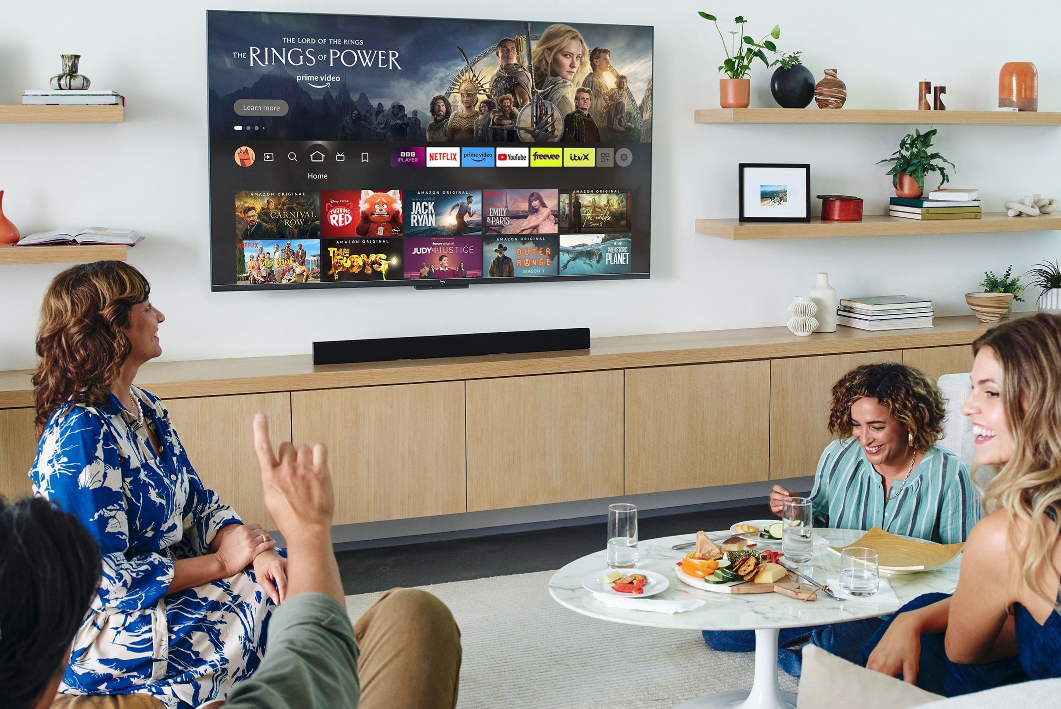 a group of people sit around a sofa watching an amazon fire tv omni series mounted on the wall