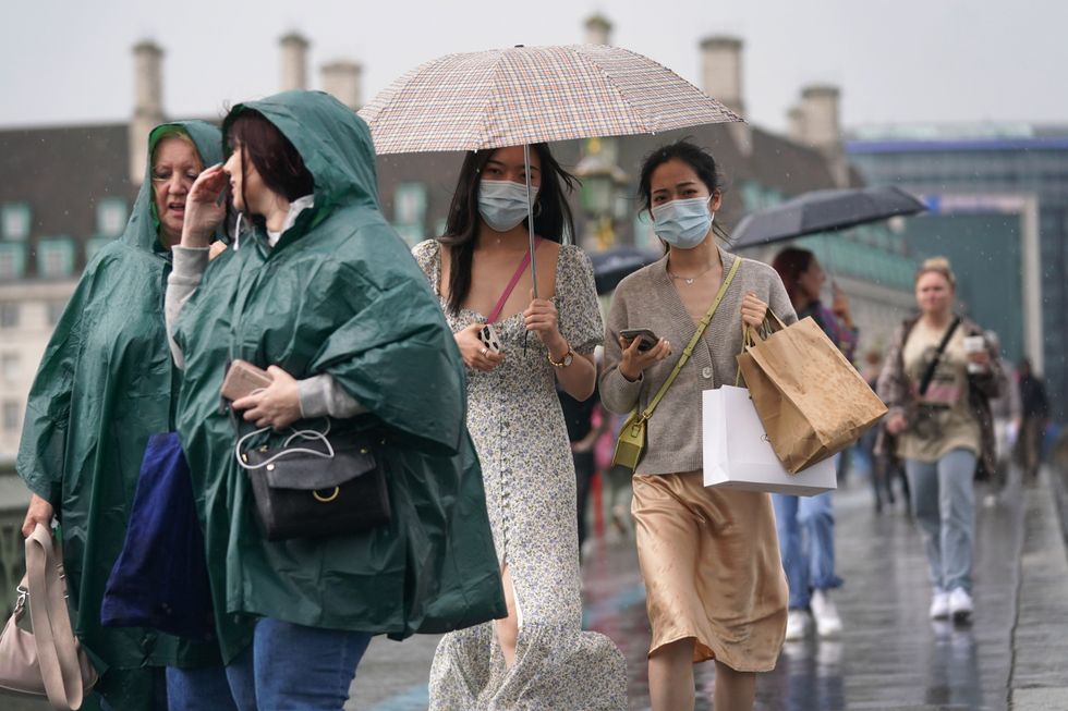 A group of people walk over Westminster Bridge as heavy rain sweeps through central London. Thunderstorms bringing lightning and torrential rain to the south are set to continue until Monday, forecasters have said. Picture date: Sunday July 25, 2021.
