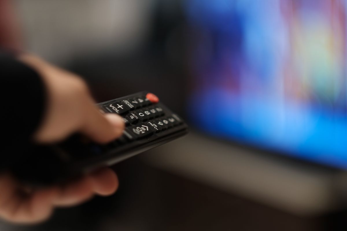 a hand holding a remote control changes the channel on a tv that's out-of-focus in the background 