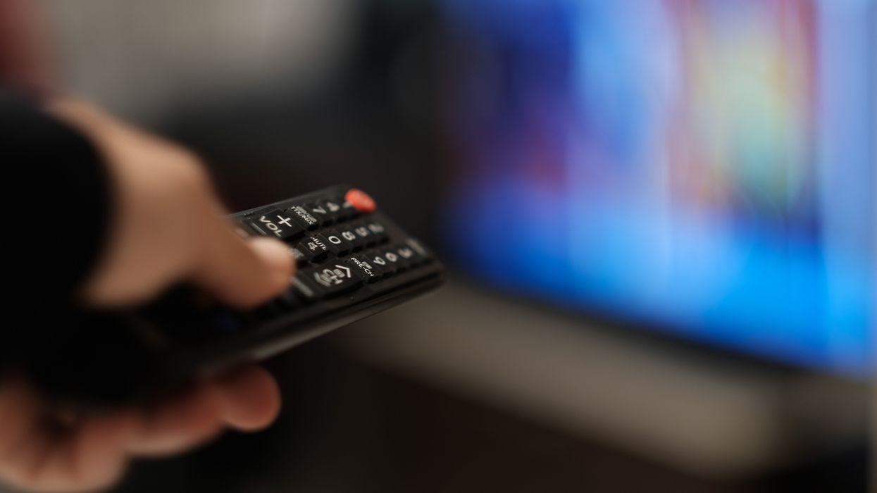 a hand holding a remote control changes the channel on a tv that's out-of-focus in the background