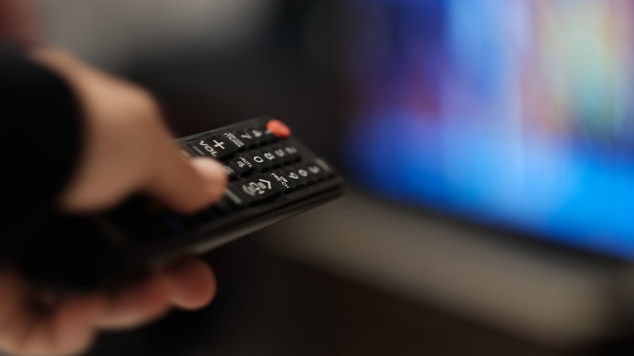 a hand holding a remote control changes the channel on a tv that's out-of-focus in the background