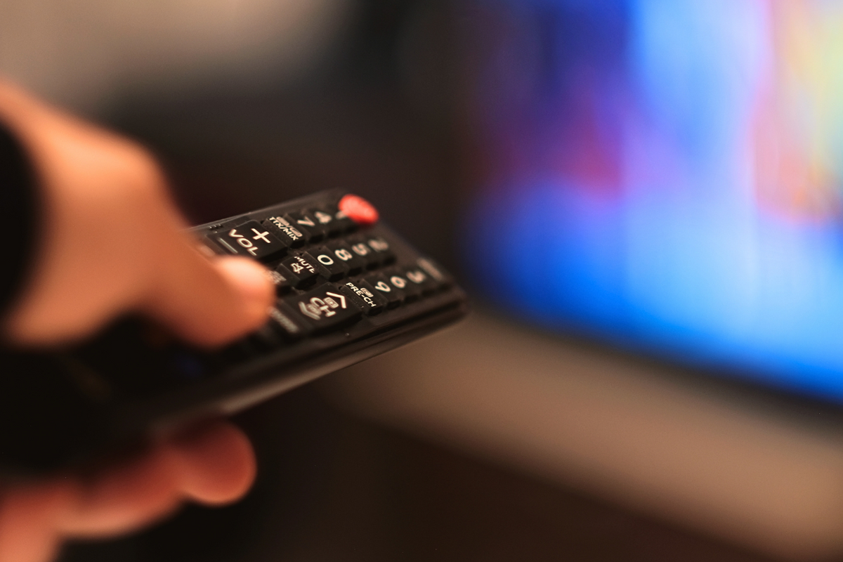 a hand holding a remote control pointed at a television that's out of focus 