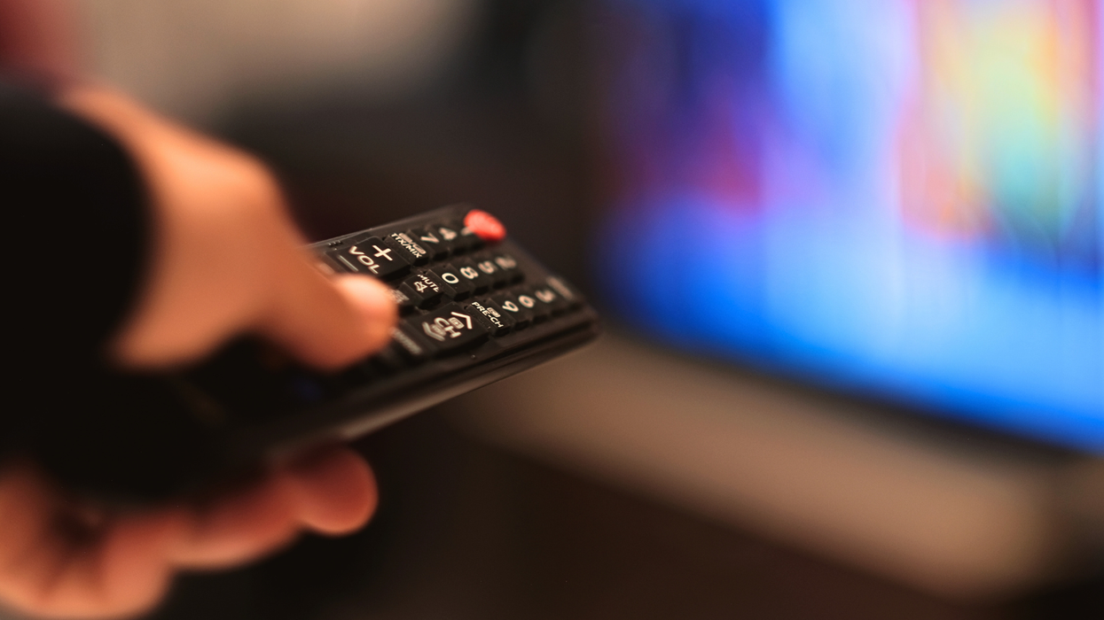 a hand holding a remote control pointed at a television that's out of focus