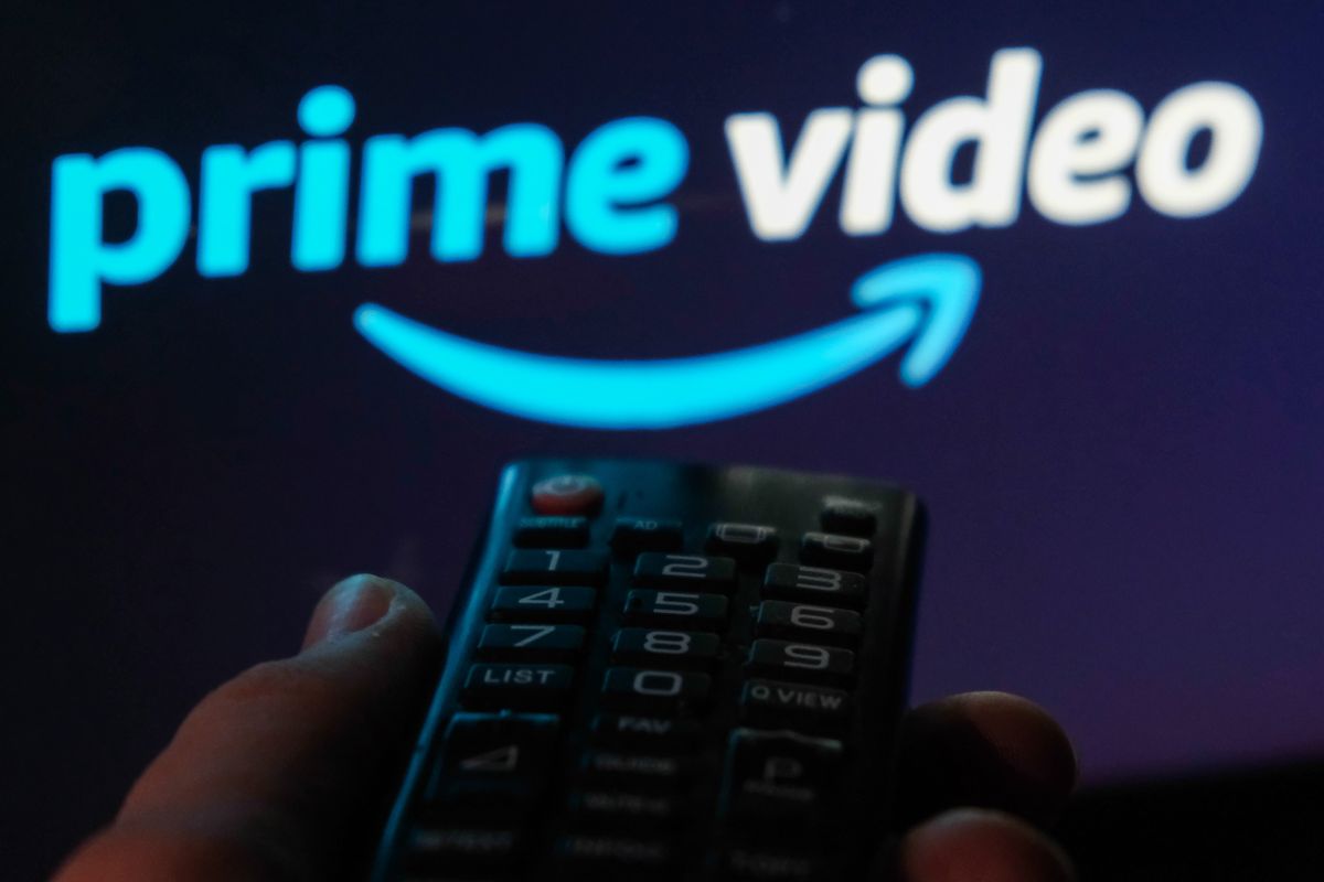 a hand holding a remote control points at a flatscreen tv with the prime video logo on it  