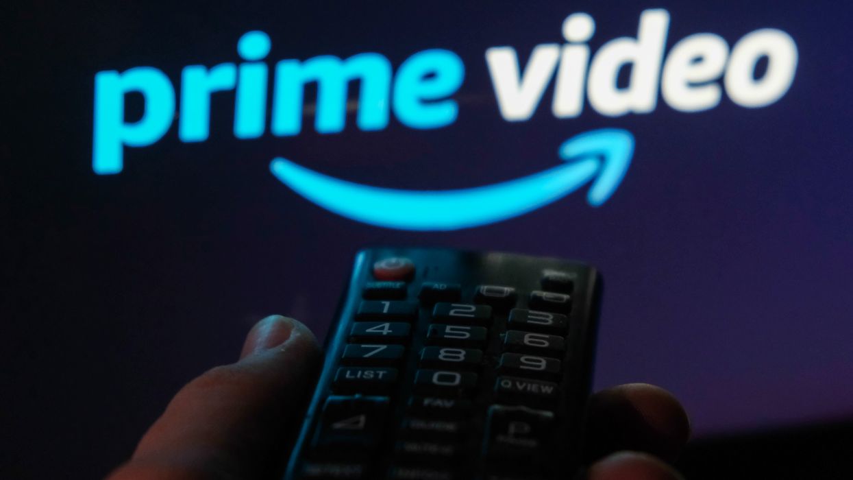 a hand holding a remote control points at a flatscreen tv with the prime video logo on it