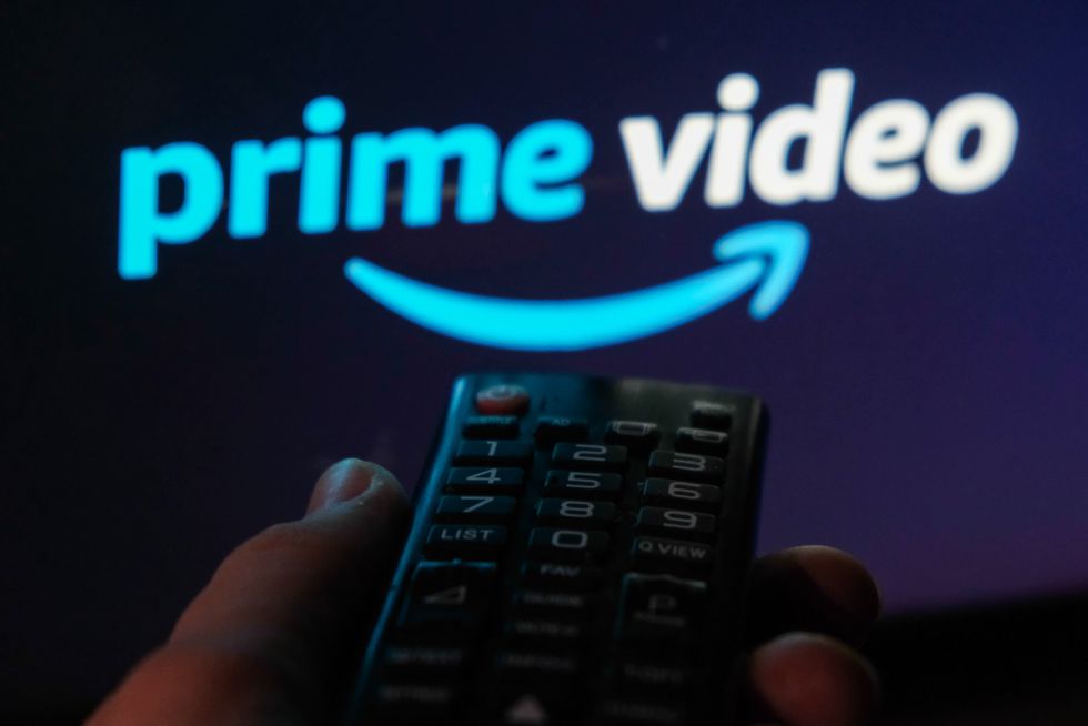 a hand holding a remote control points at a flatscreen tv with the prime video logo on it