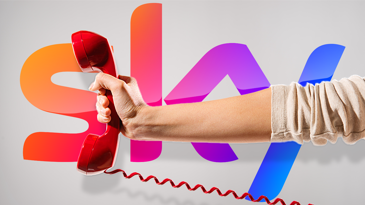 a hand holds a landline phone with the sky tv logo in the background
