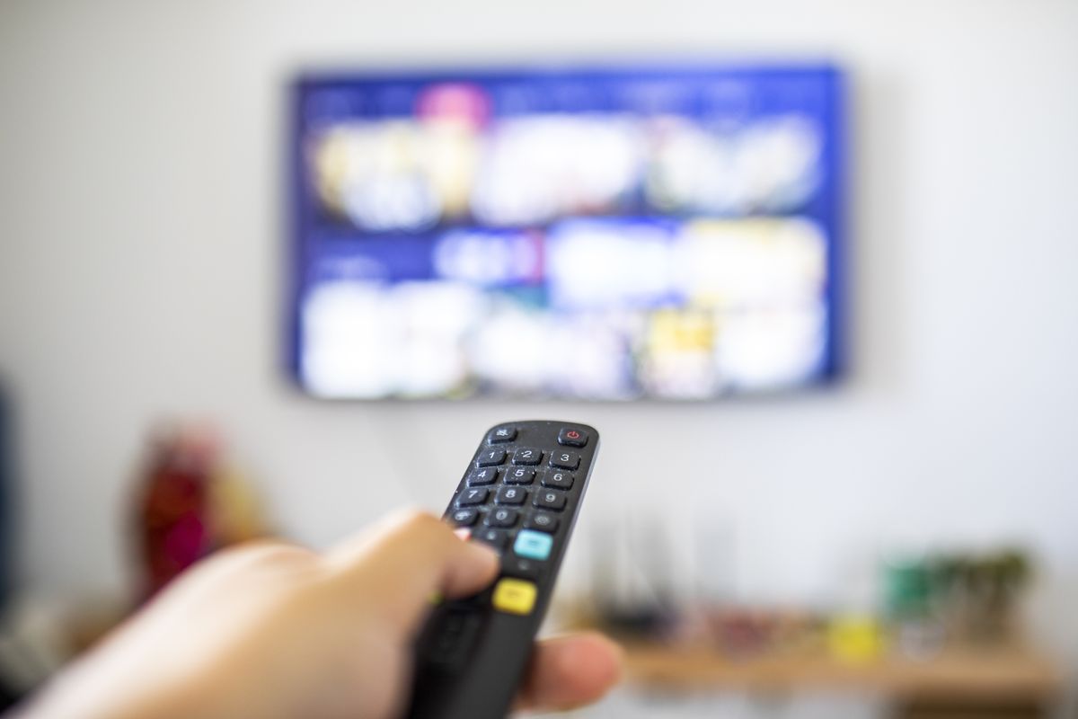 a hand holds a remote control pointed at the television screen  