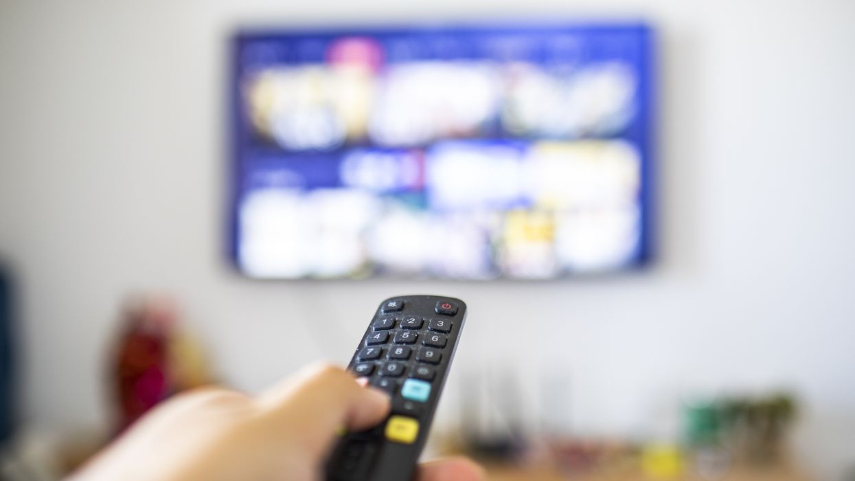 a hand holds a remote control pointed at the television screen