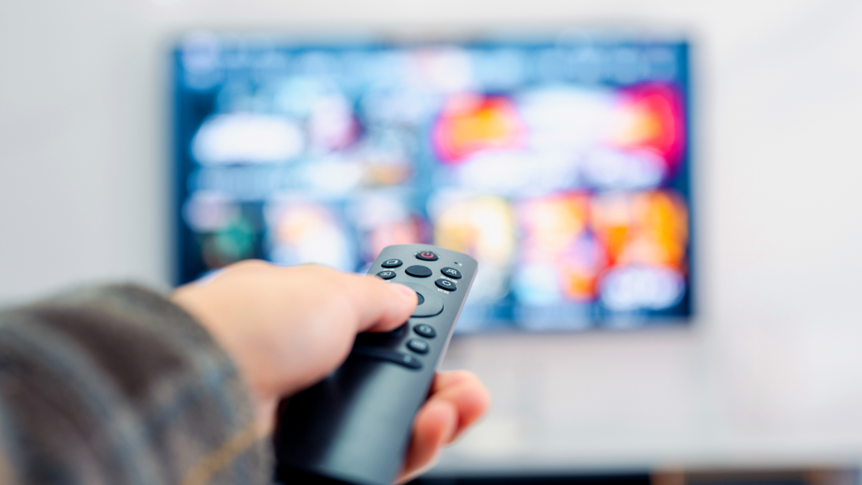 a hand holds a remote control pointing at a television screen