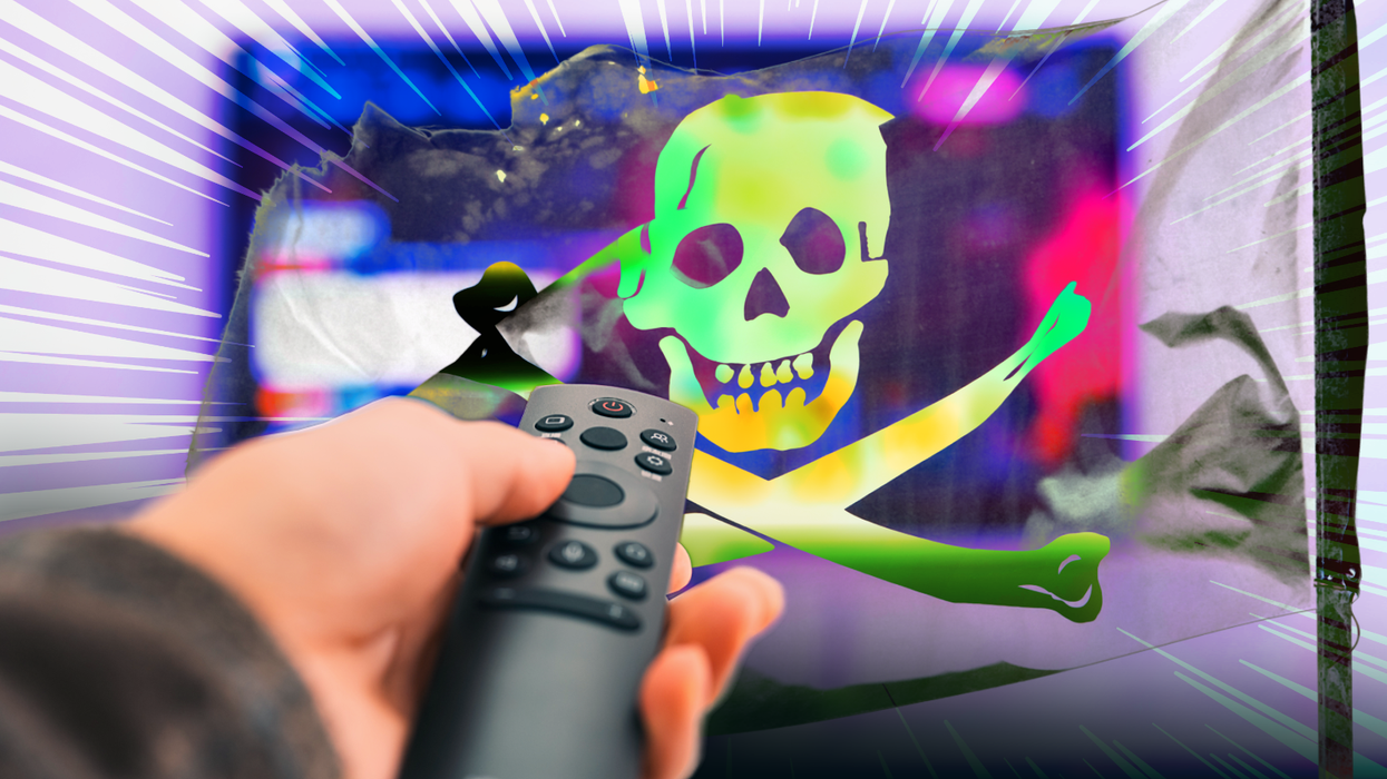 a hand holds a remote control with a television in the background visible through a pirate flag