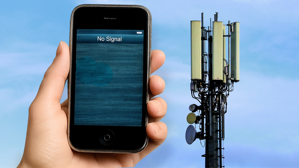 a hand holds a smartphone showing no signal with a 3g mast in the background