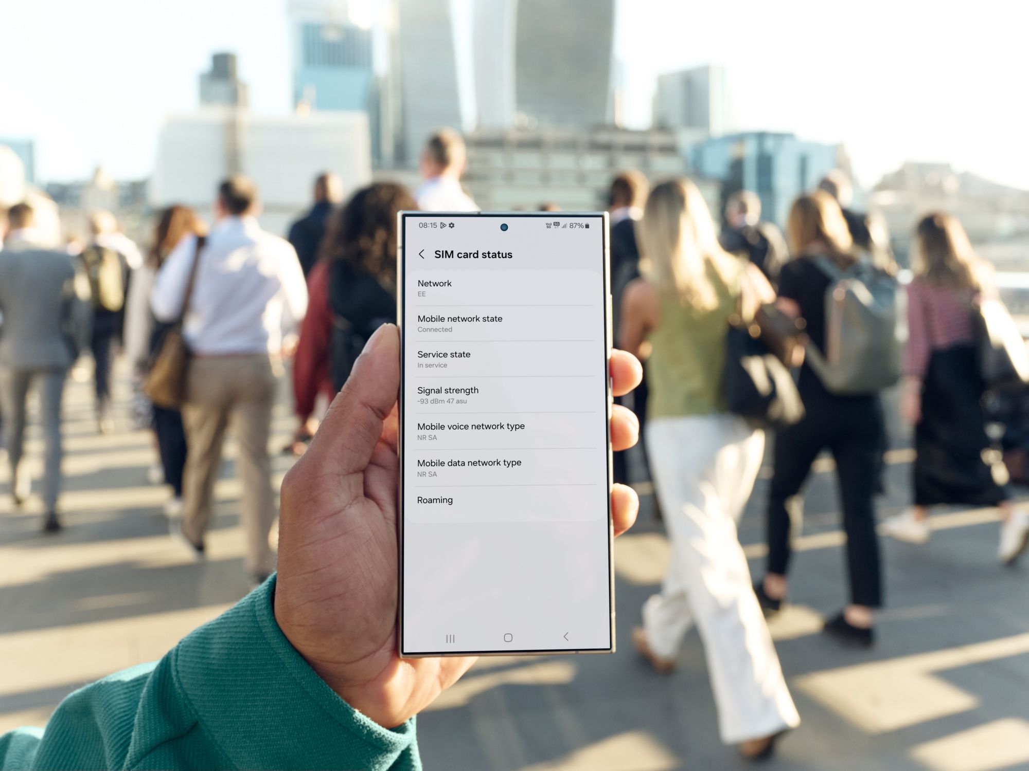 a hand holds a smartphone showing the settings screen on a busy street