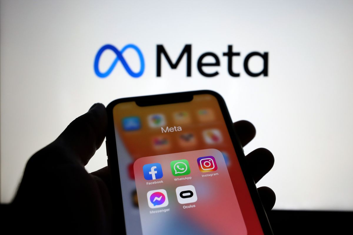 a hand holds a smartphone with a folder of apps owned by meta including instagram facebook whatsapp and messenger