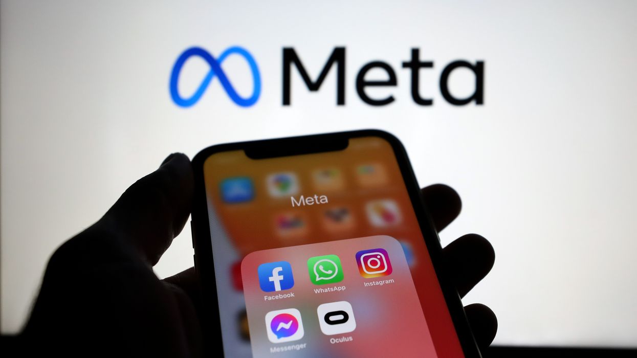 a hand holds a smartphone with a folder of apps owned by meta including instagram facebook whatsapp and messenger