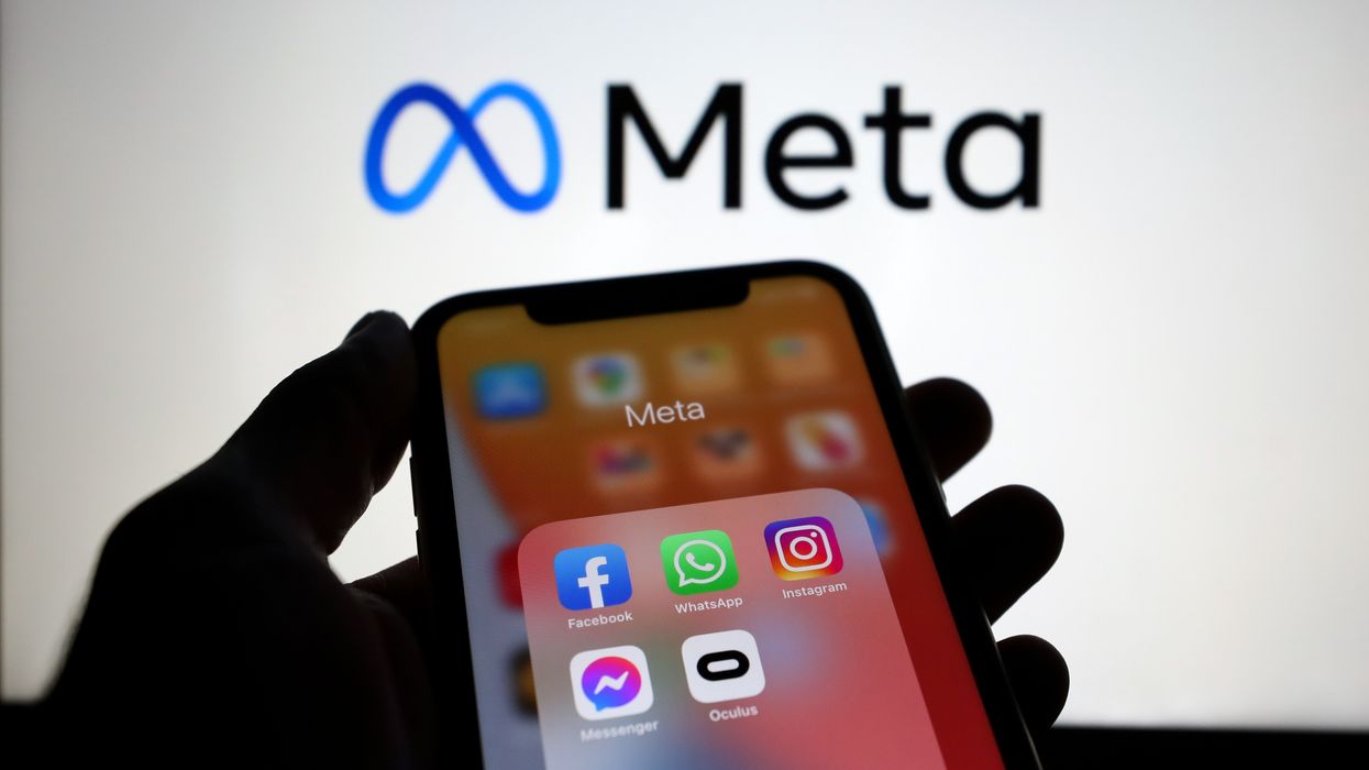 a hand holds a smartphone with a folder of apps owned by meta including instagram facebook whatsapp and messenger