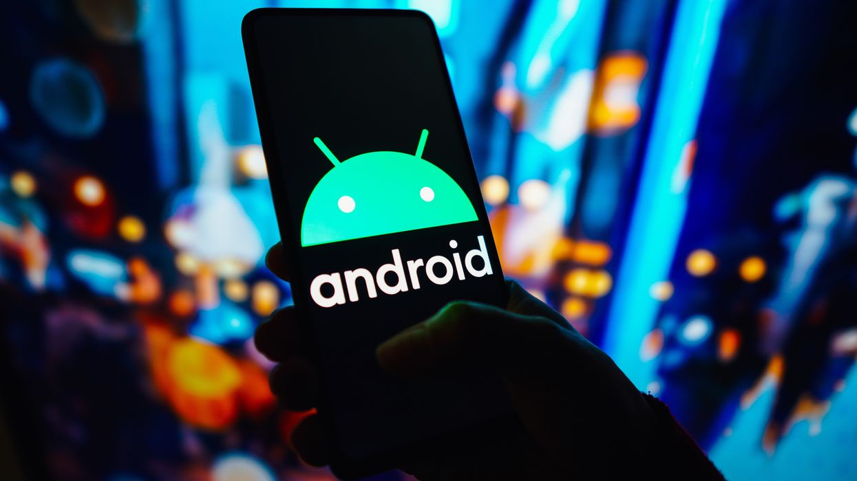 a hand holds a smartphone with the android operating system logo pictured on screen