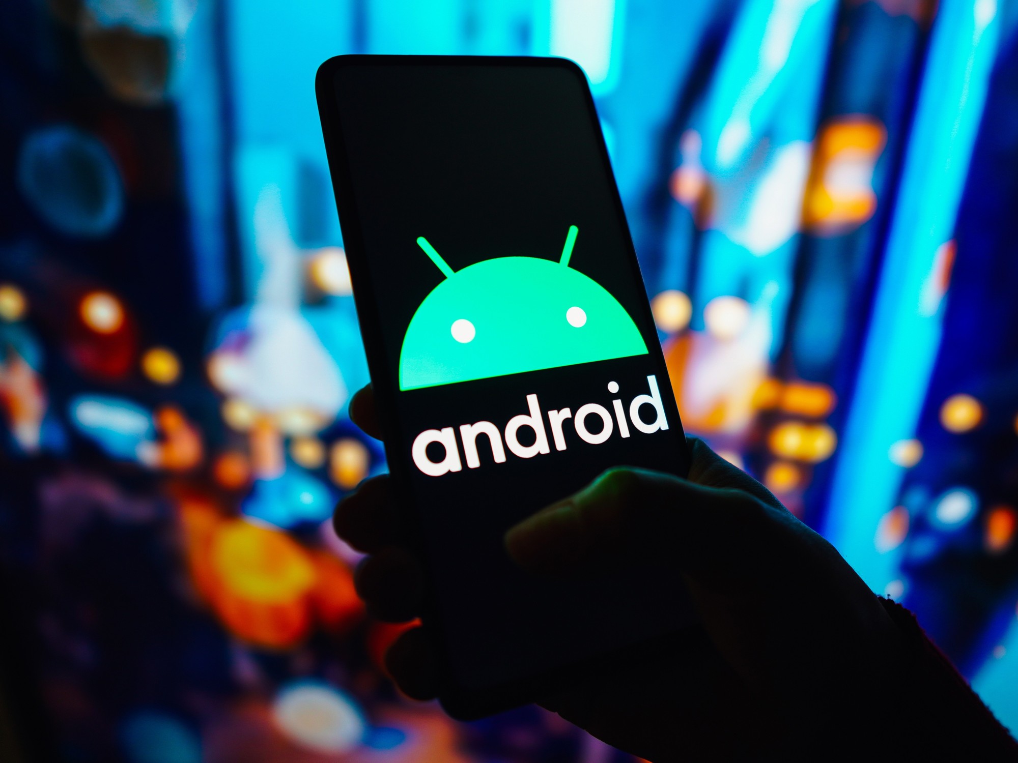 a hand holds a smartphone with the android operating system logo pictured on screen