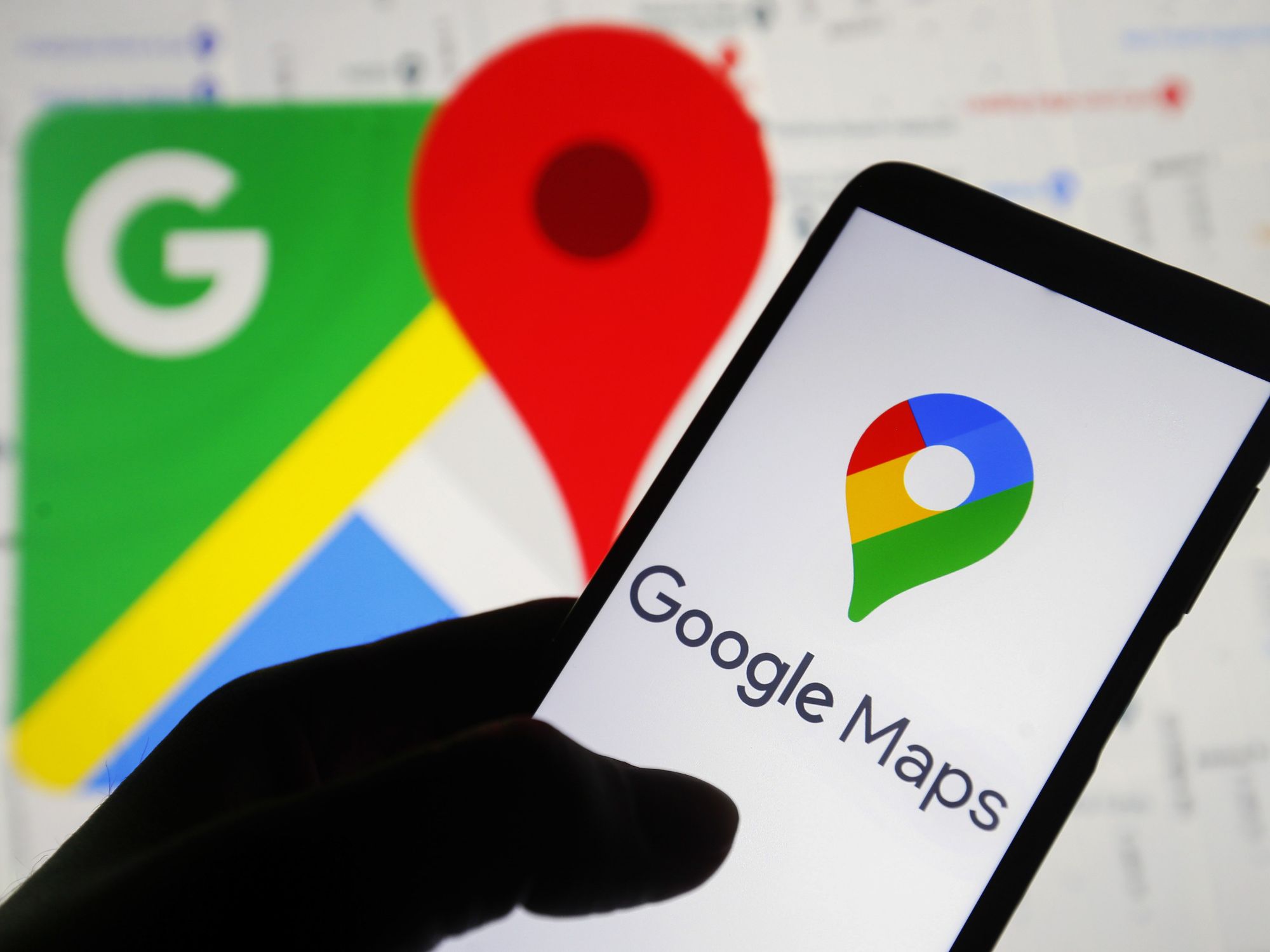 a hand holds a smartphone with the google maps icon on-screen