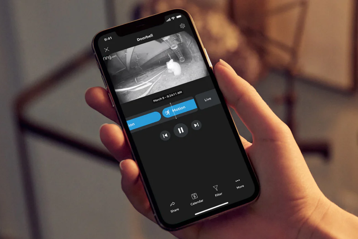 a hand holds a smartphone with the ring app installed reviewing security footage