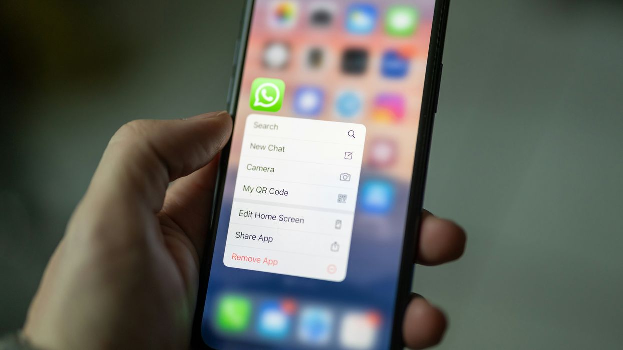 a hand holds a smartphone with the whatsapp app icon on the homescreen