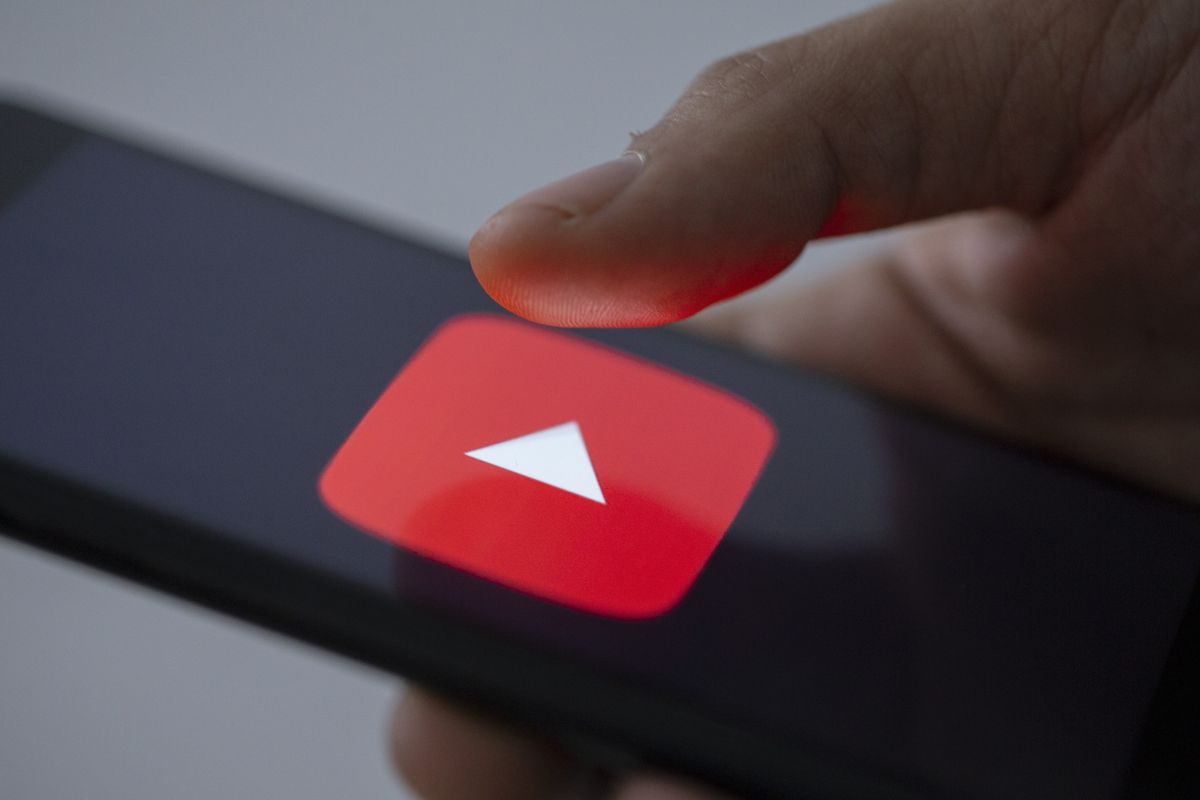 a hand holds a smartphone with the youtube logo on-screen  