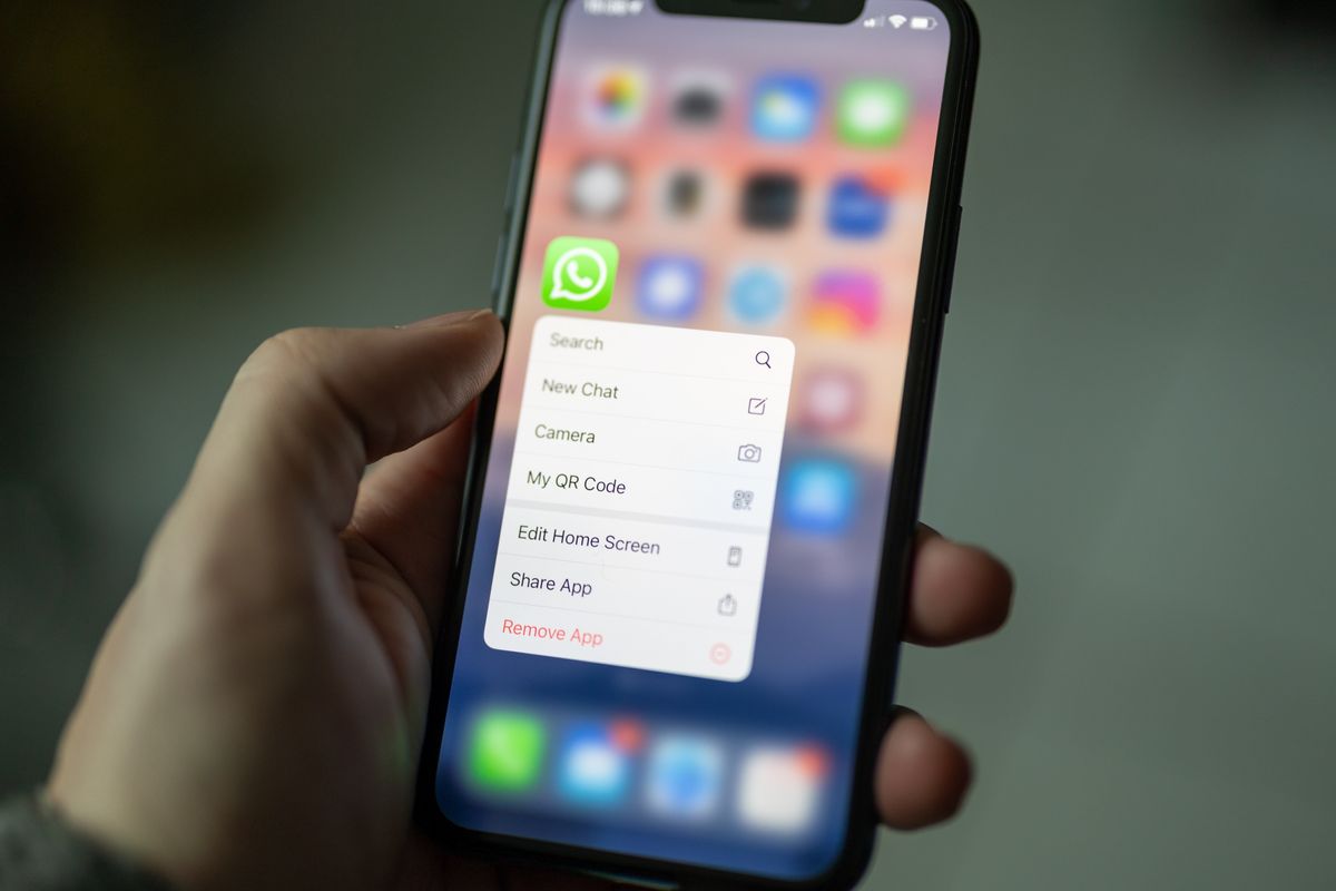 a hand holds an iphone with the whatsapp app icon prominently displayed on-screen 