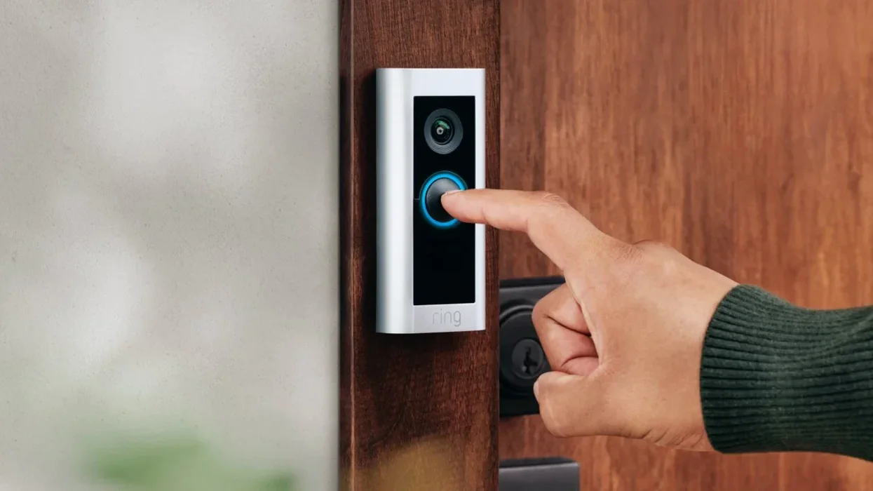 a hand is seen pressing a ring doorbell fitted to a wooden frame
