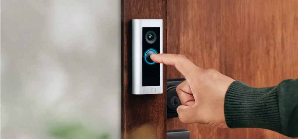 a hand is seen pressing a ring doorbell fitted to a wooden frame 