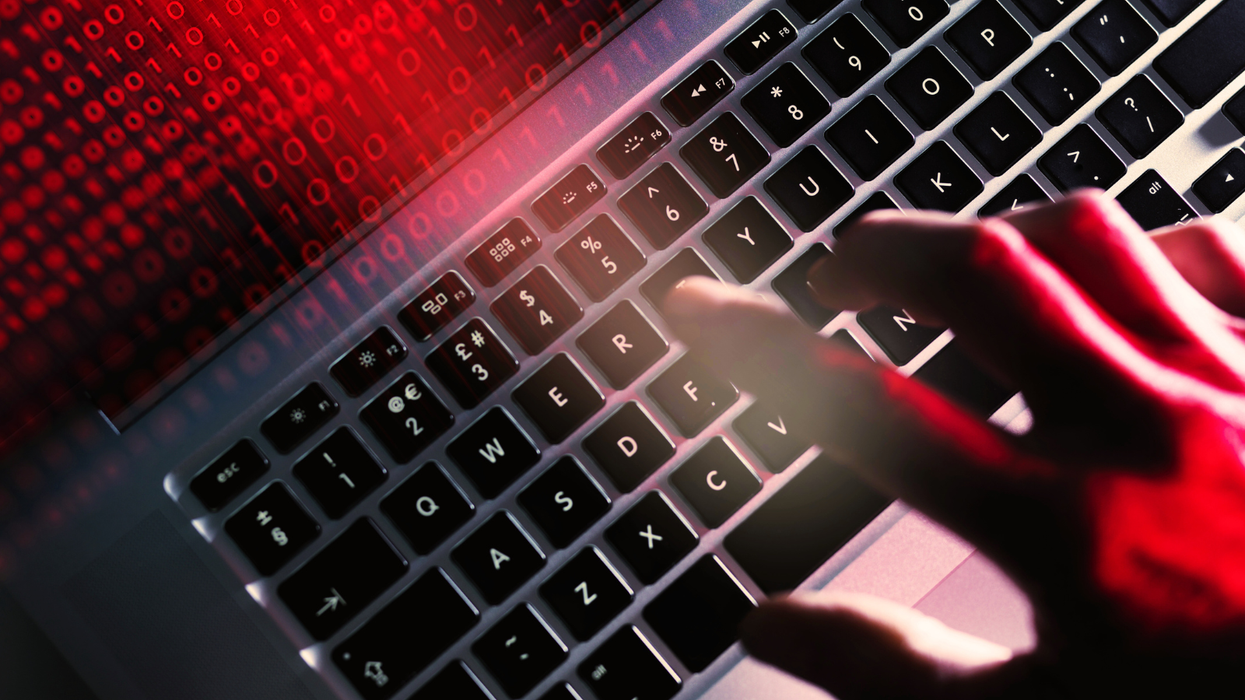 a hand is seen typing on a keyboard with bright red computer code bleeding out from the screen