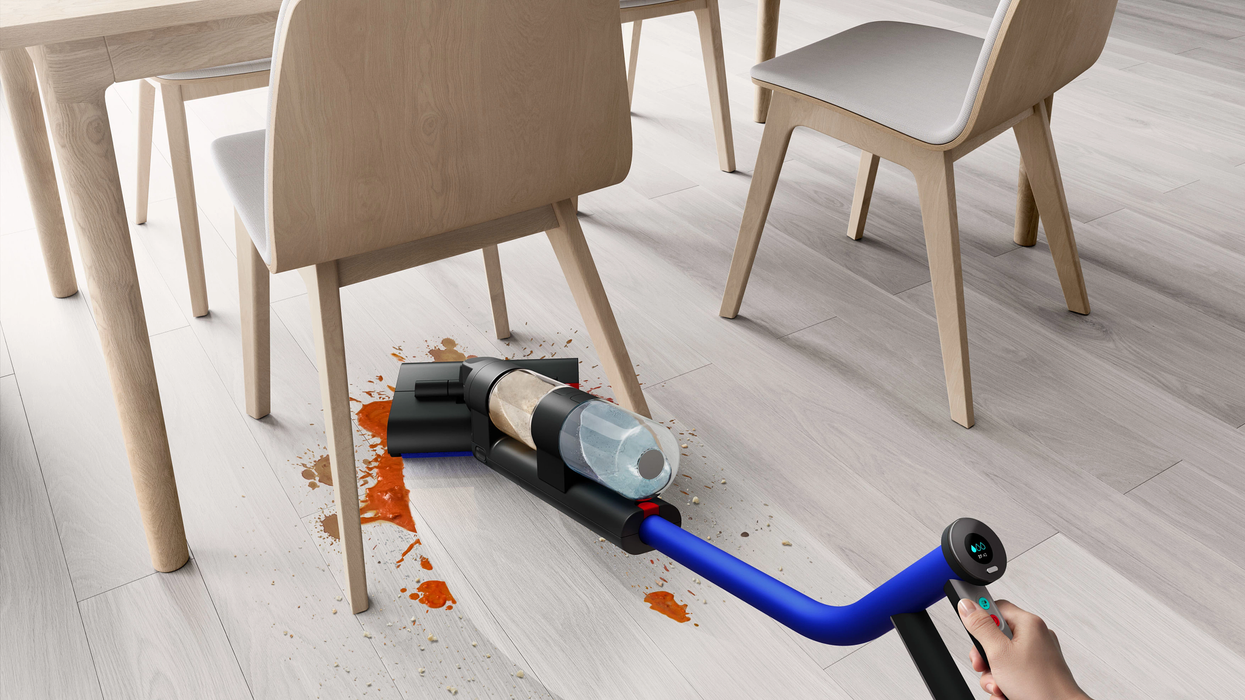 a hand manoeuvres the Dyson Wash G1 wet floor cleaner under a seat using the omni-glide casters