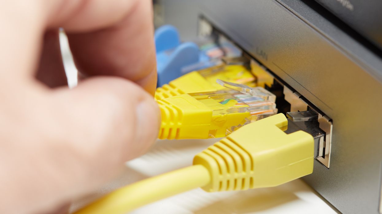 a hand plugs an ethernet cable into the back of a wifi router