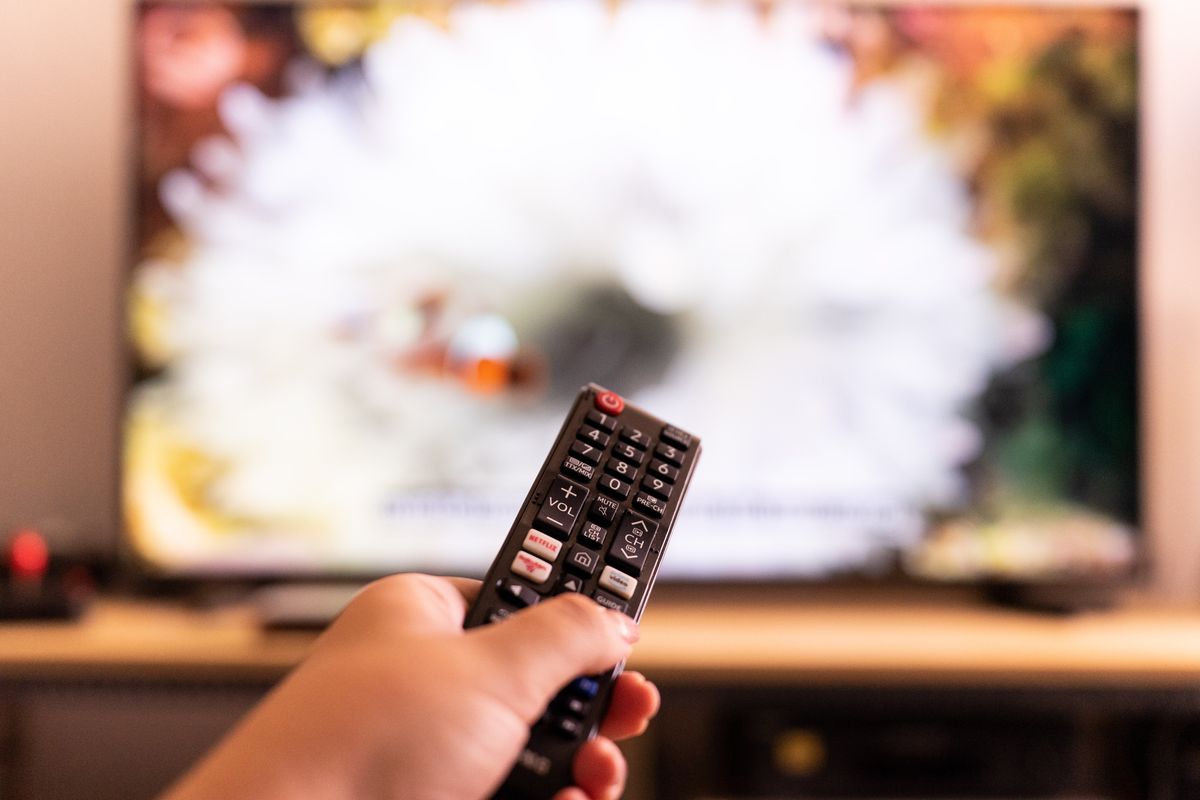 a hand points a remote control at a tv with a blurred image on-screen
